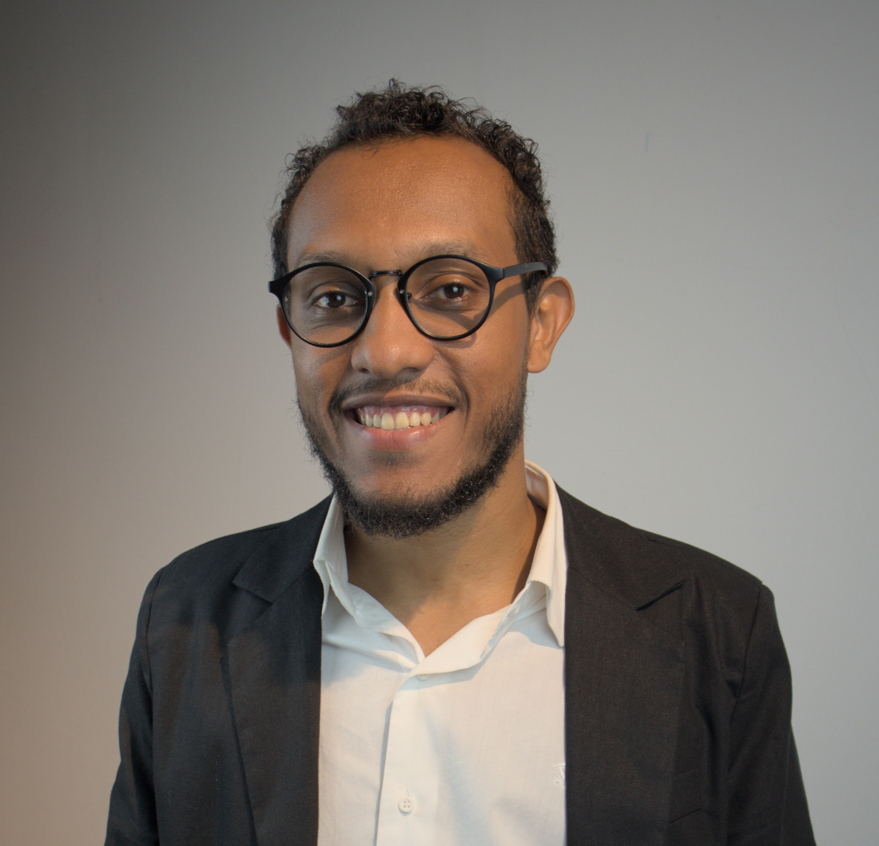 Foto de Adriel de óculos, terno e com um sorriso